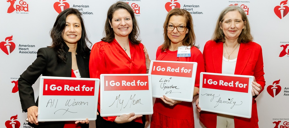 Four women dressed in red holding up dry erase boards that read I Go Red for all women, my mom, Lori, and my family.